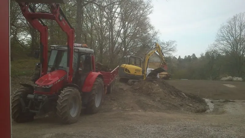 Röd traktor med lastare och grävmaskin på arbetsplats